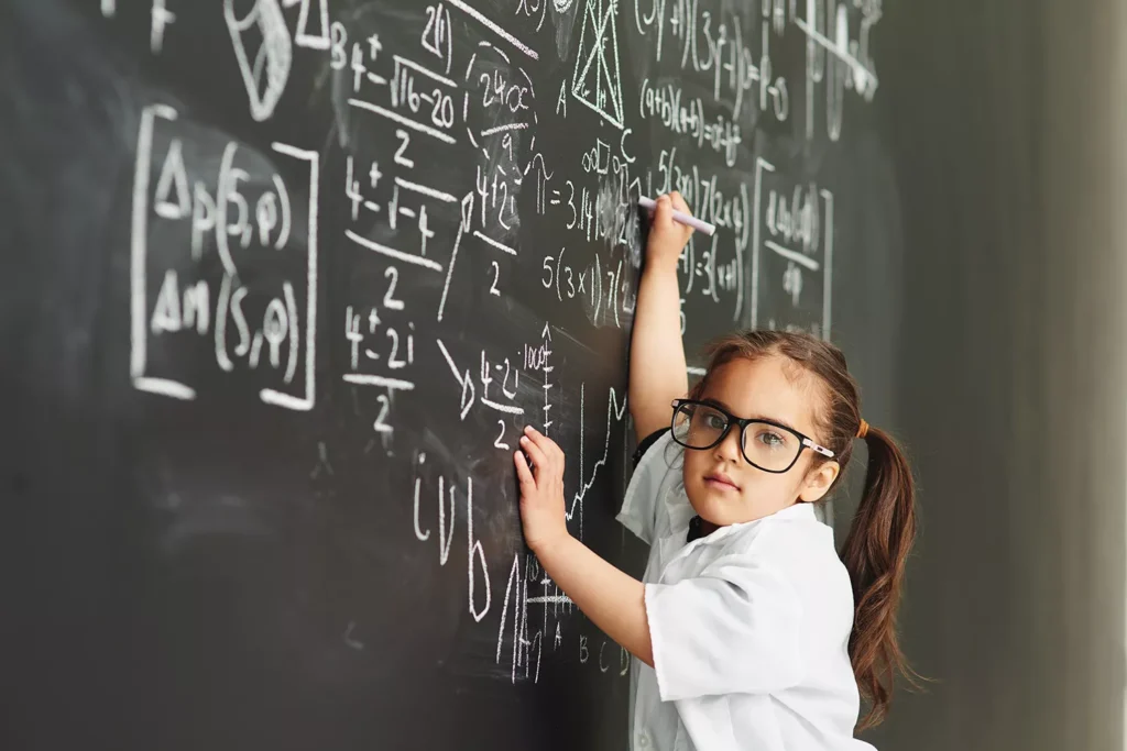 Menina pequena gênia escrevendo fórmulas complexas de matemática em uma lousa