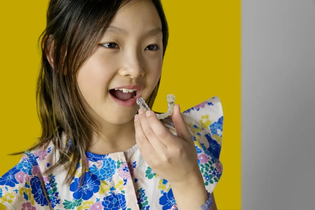 Menina colocando o aparelho Invisalign na boca - Just Real Moms