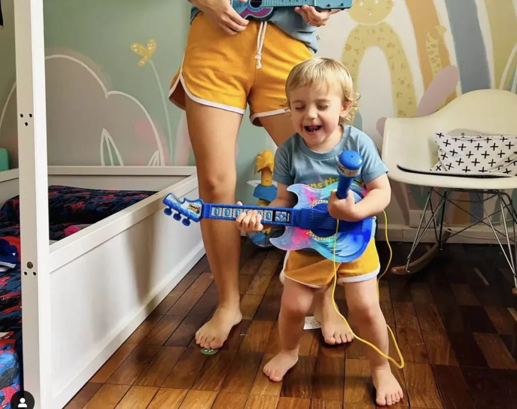 Bebê menino brincando de tocar guitarra com mãe em quarto vestindo roupas da Studio Pipoca - Just Real Moms