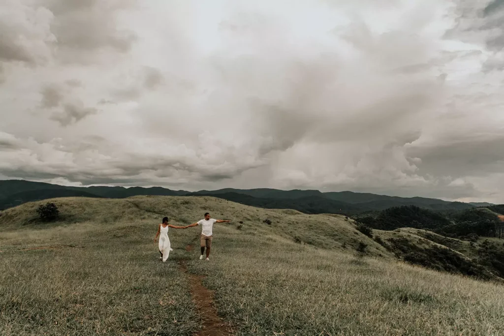 Casal, Homem e mulher, de mãos dadas andando em campo aberto com céu parcialmente nublado - Just Real Moms