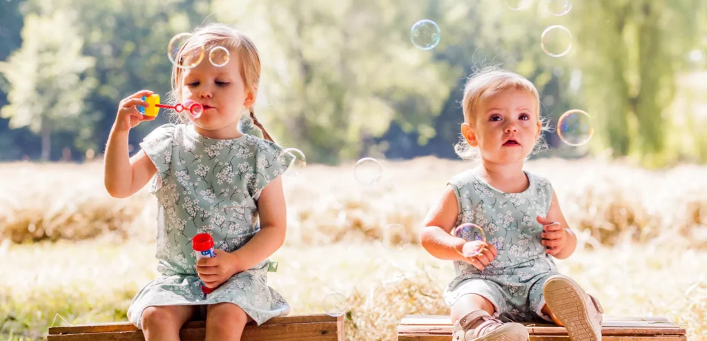 Duas meninas vestindo Mimor Kids sentadas em área externa com campo verde ao fundo