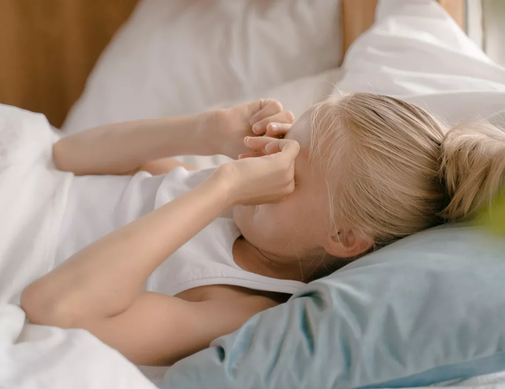 Menina pequena deitada na cama, coçando os olhos com Conjuntivite alérgica - Just Real Moms