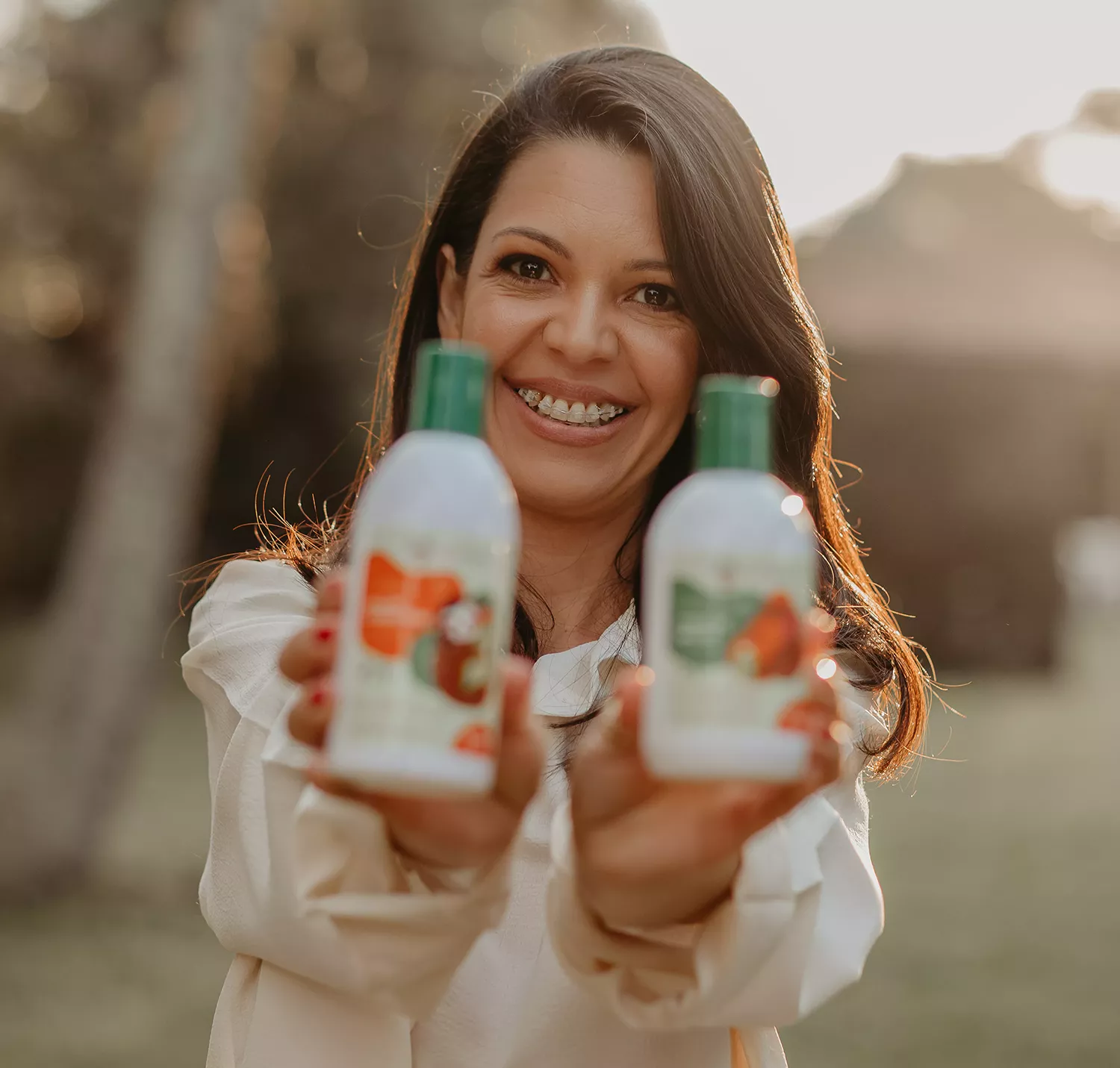 Fundadora, Estefânia Peixoto, posando para a câmera segurando dois produtos da sua linha da Afeto Natural - Just Real Moms