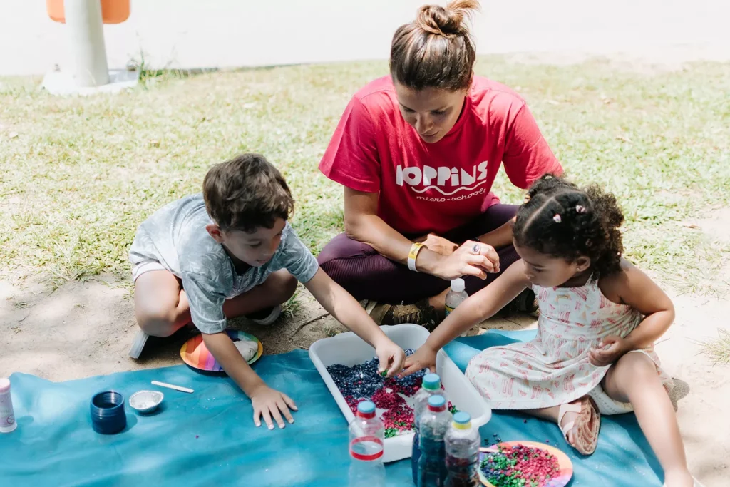 Educadora com duas crianças em tapete brincando com crianças em área externa