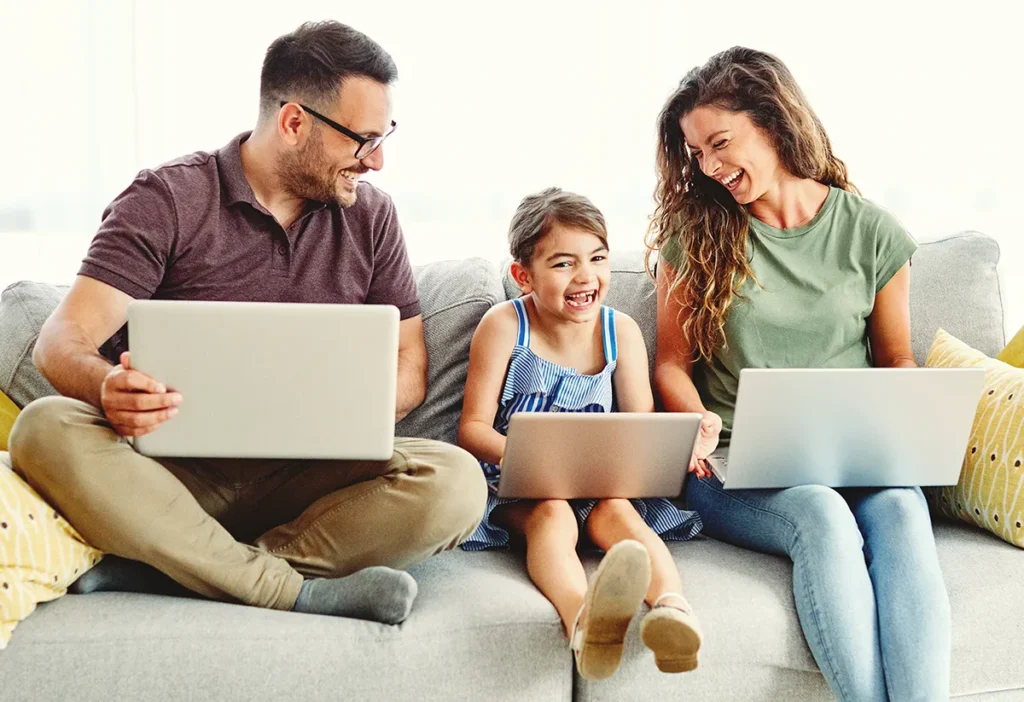 Mãe, pai e filha no sofá, todos com computador fazendo compras de Black Friday