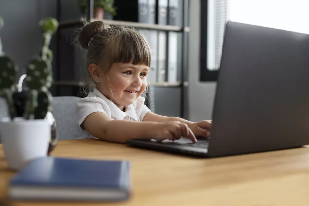 Menina pequena sentada em frente a um computador digitando e sorrindo