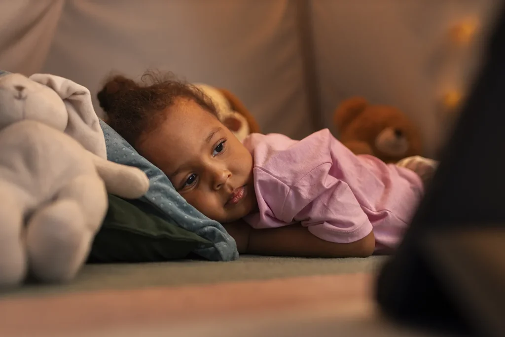 Menina pequena deitada no sofá ao lado de um coelhinho de pelúcia