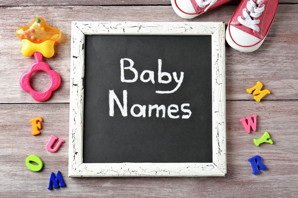 Lousa de gis escrito em inglês "Baby Names" com letras ao lado e um para de Converse kids vermelho