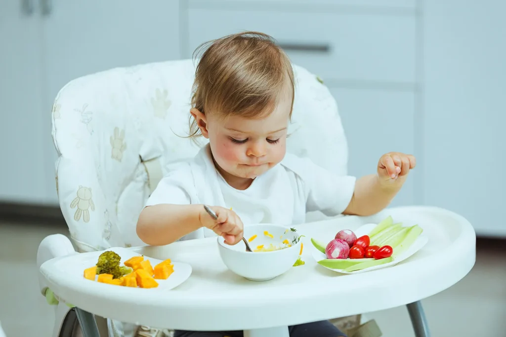 Bebe pequeno em cadeirinha de alimentação comendo no seu momento de introdução alimentar