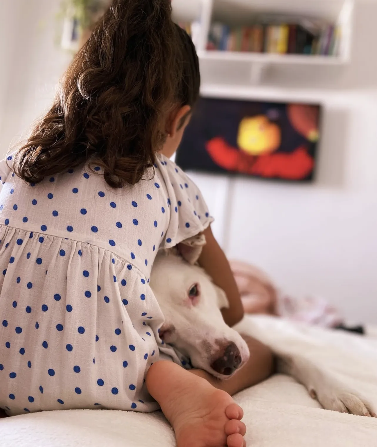 Menina na cama, com cachorro grande deitado em seu colo