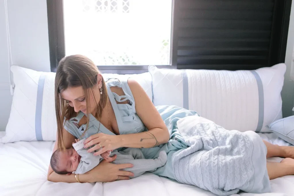 Mãe segurando bebê recém-nascido nos braços, deixados na cama