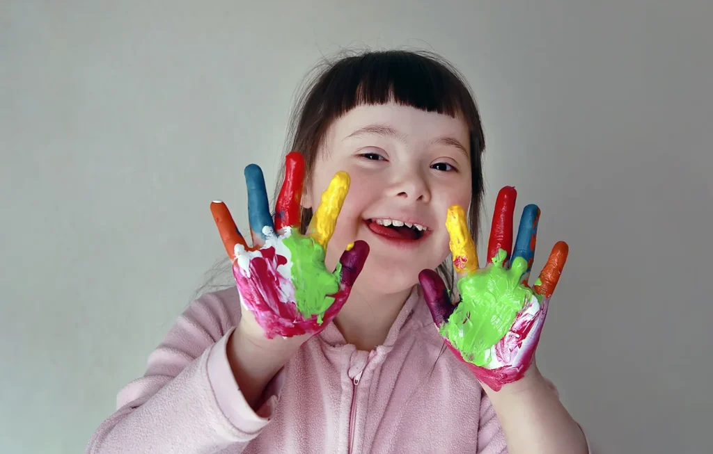 Menina sorrindo com Síndrome de Down e mãos pintadas