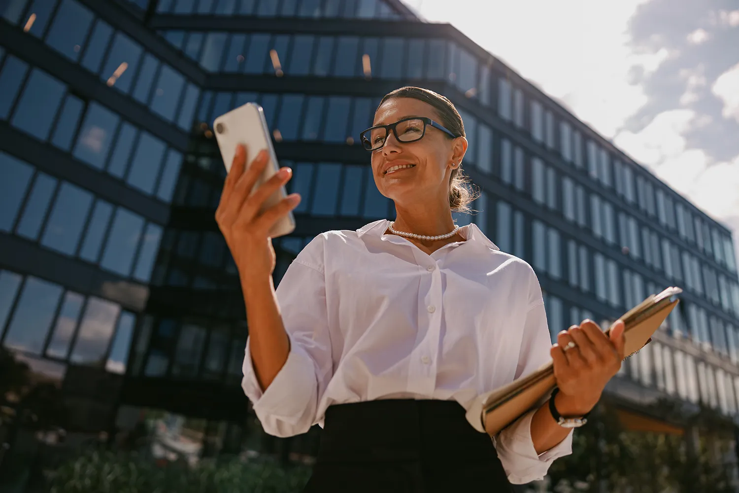 Empreendedora segurando celular na frente de um grande escritório - Redes Sociais: Estratégia de Vendas e Conexão para o Mercado Infantil
