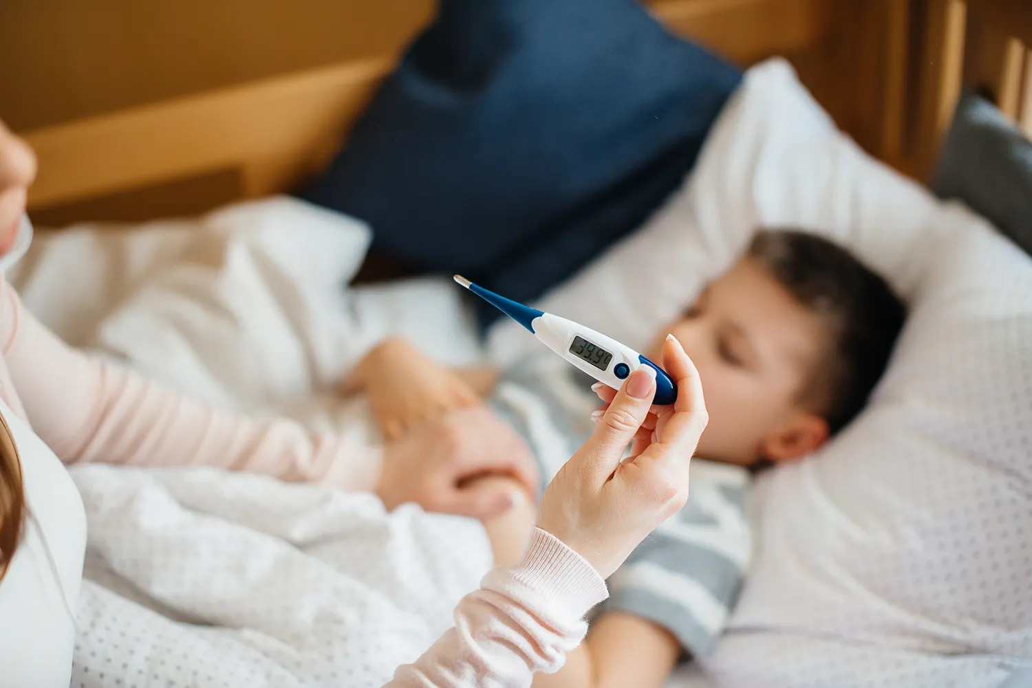 Menino doente deitado na cama com mãe tirando temperatura com termômetro