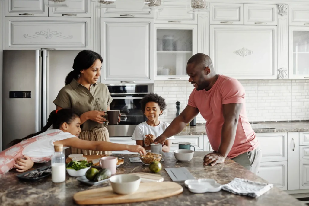 Pai, mãe e filhos reunidos na cozinha fazendo atividades em família