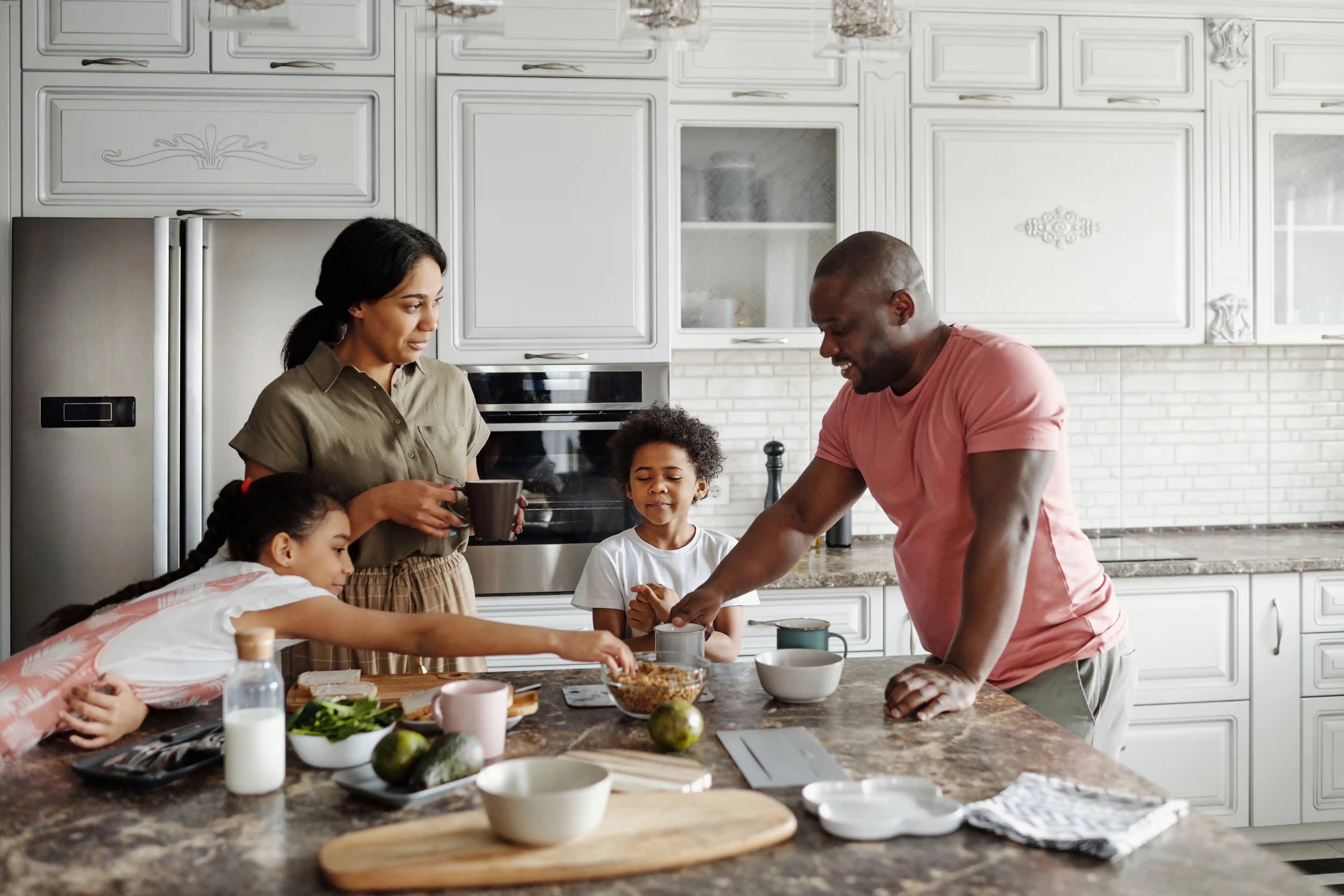 Pai, mãe e filhos reunidos na cozinha fazendo atividades em família