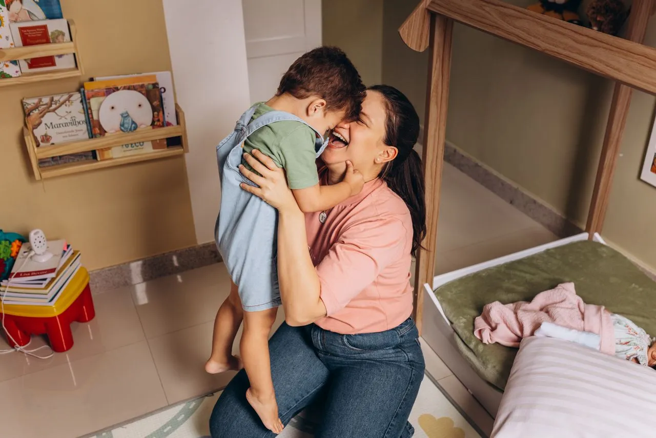 mãe abraça o filho pequeno em um momento de carinho no quarto infantil, representando a construção de vínculos e aprendizados desde a infância para criar uma relação com filho adolescente no futuro