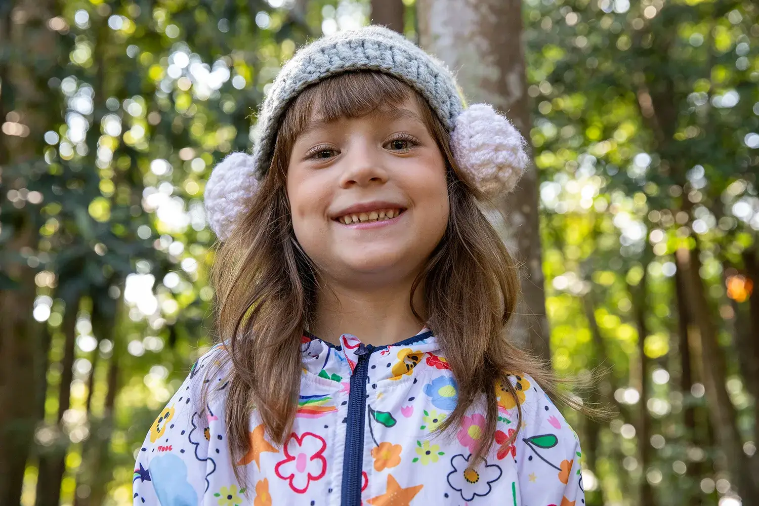Menina de gorro de tricot e casado corta vento branco com estampas em campanha da marca infantil Jooba