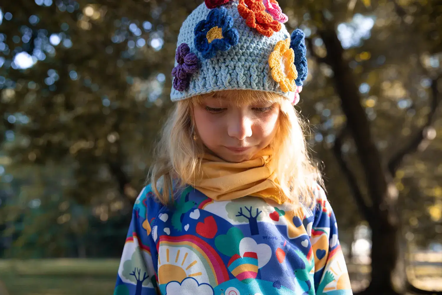 Menina com gorro de tricot com flores e moletom colorido em campanha da marca infantil Jooba