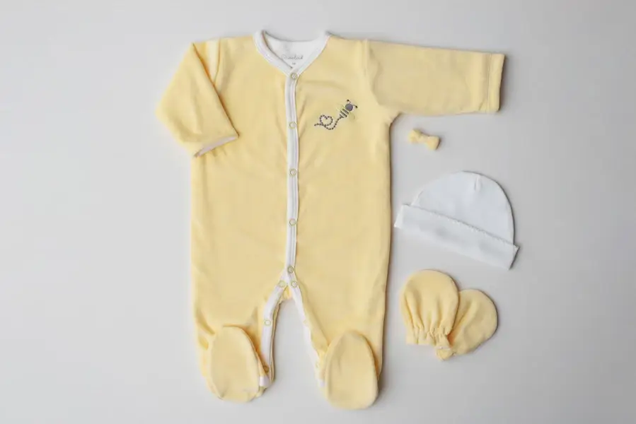 Pijama infantil de plush amarelo com acessórios ao lado - lacinho, gorro e luva - Just Real Moms