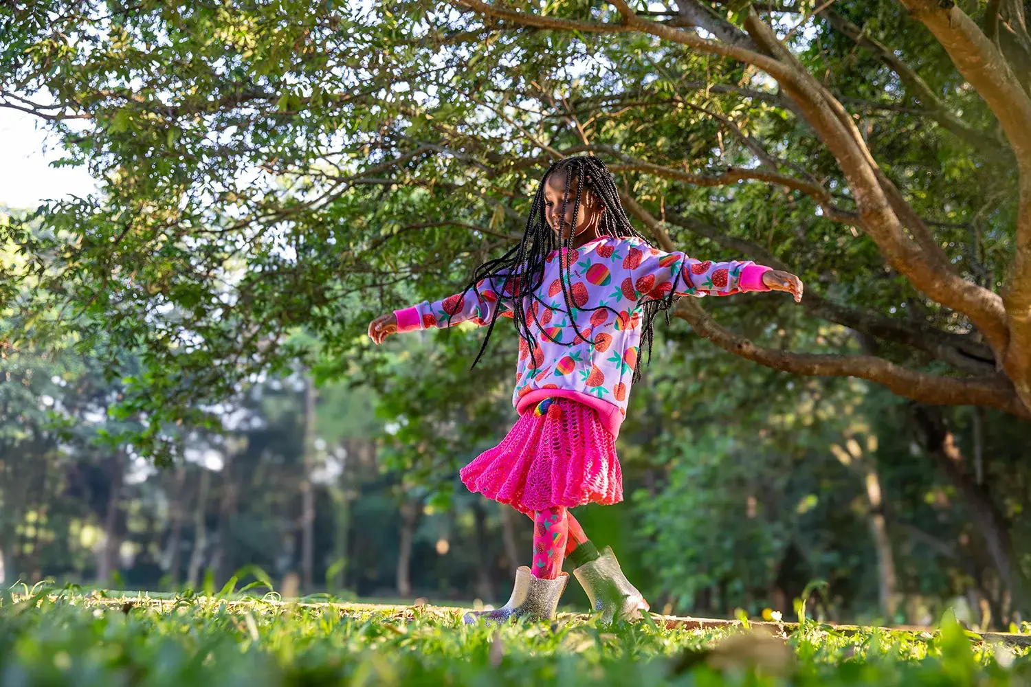 Menina usando moletom de morangos coloridos, saia de tricot infantil pink e galocha transparente em campanha da marca infantil Jooba
